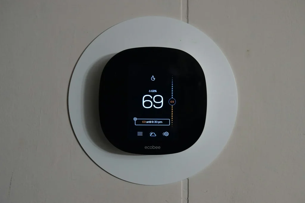 A close-up of a modern thermostat mounted with its screen displaying the temperature set to 69 degrees.