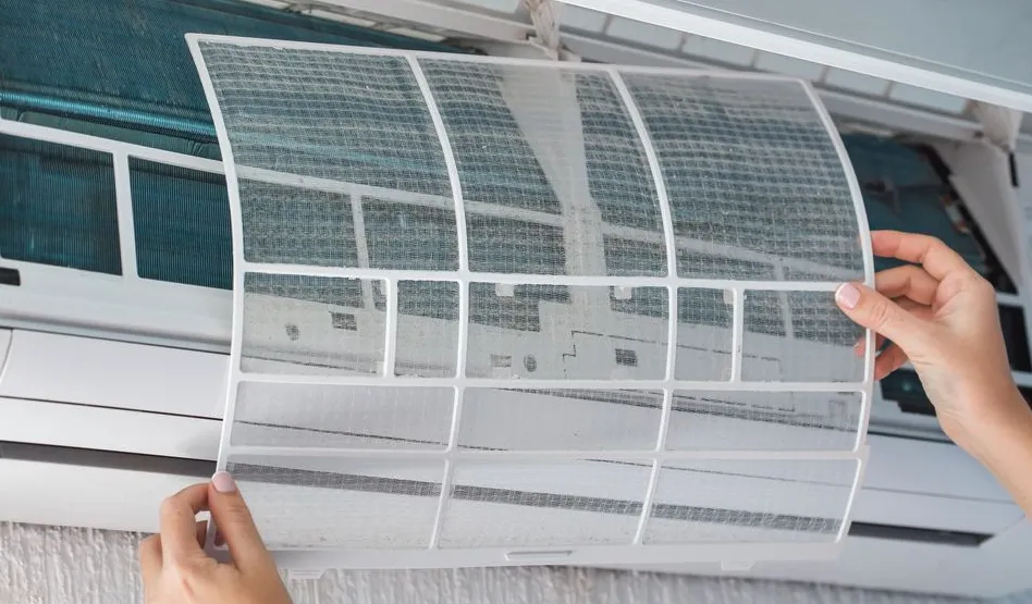 A photo of hands removing a dirty air filter from an indoor AC unit