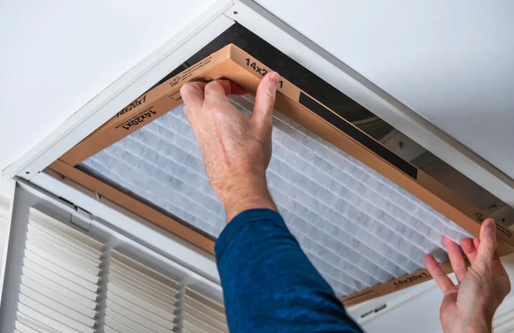 A person changes an AC air filter. To make AC units last longer, regular maintenance like this is essential for a long lifespan
