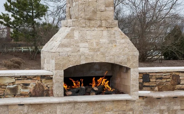 A gas fireplace made from paving stone burning outside on a patio