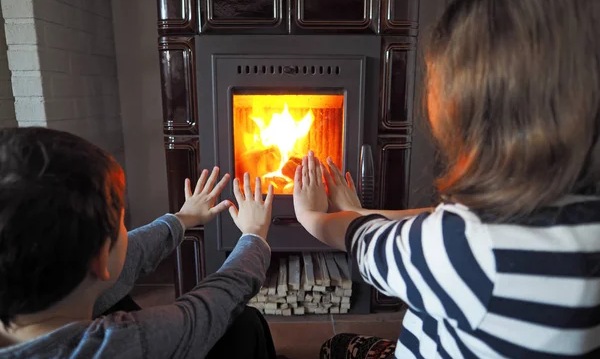 Two little kids warm up by the fireplace